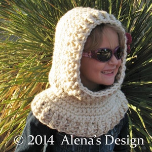 May include: A cream-colored, crocheted hood and cowl set. The hood features a rounded top and a wide, ribbed cowl that sits around the neck. The design is handmade with a textured stitch. The text "&copy; 2014 Alena's Design" is visible at the bottom.