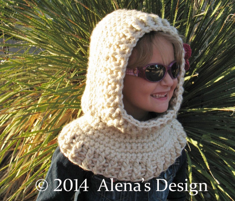 May include: A cream-colored, crocheted hood and cowl set. The hood features a rounded top and a wide, ribbed cowl that sits around the neck. The design is handmade with a textured stitch. The text "&copy; 2014 Alena's Design" is visible at the bottom.