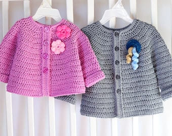 May include: Two crocheted baby cardigans, one pink with pink flower embellishments and one gray with blue and yellow flower embellishments.