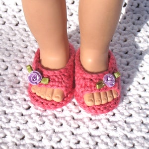 K&ouml;nnte beinhalten: Ein Paar rosa geh&auml;kelte Sandalen mit lila und gr&uuml;nen Blumenverzierungen.