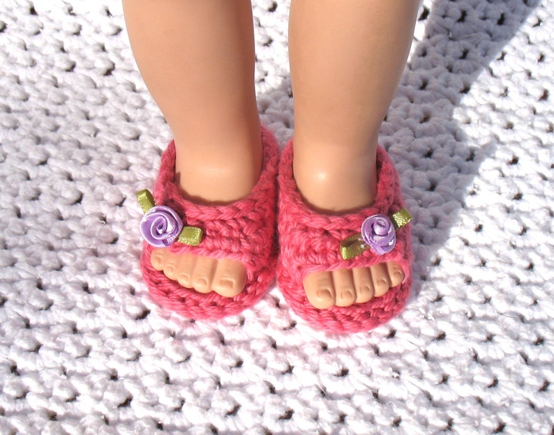 K&ouml;nnte beinhalten: Ein Paar rosa geh&auml;kelte Sandalen mit lila und gr&uuml;nen Blumenverzierungen.