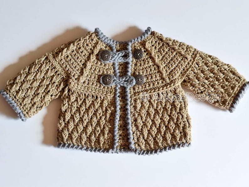 May include: A crocheted baby cardigan in a beige color with gray trim and silver buttons. The cardigan has a textured stitch pattern and a slightly flared shape.