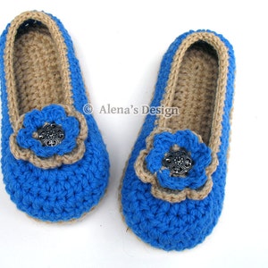 Puede incluir: Un par de zapatillas de crochet azul y beige con un adorno de flor y un botón plateado en el centro.