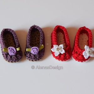 Puede incluir: Dos pares de zapatos de bebé tejidos a crochet. Un par es morado con una flor morada y una cinta verde. El otro par es rojo con una flor blanca y una cinta blanca.