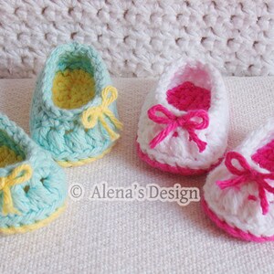 Puede incluir: Dos pares de zapatos de beb&eacute; tejidos a crochet. Un par es azul claro con ribetes y lazos amarillos. El otro par es blanco con ribetes y lazos rosas.  "Alena's Design" est&aacute; impreso en la superficie blanca.