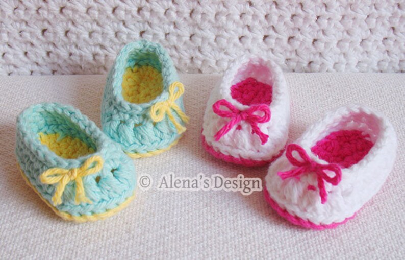 Puede incluir: Dos pares de zapatos de beb&eacute; tejidos a crochet. Un par es azul claro con ribetes y lazos amarillos. El otro par es blanco con ribetes y lazos rosas.  "Alena's Design" est&aacute; impreso en la superficie blanca.