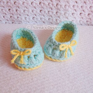 Puede incluir: Un par de zapatos de beb&eacute; tejidos a crochet en azul claro con ribetes y lazos amarillos. Los zapatos tienen un forro tejido a crochet amarillo.
