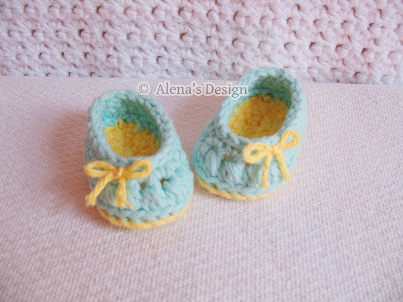 Puede incluir: Un par de zapatos de beb&eacute; tejidos a crochet en azul claro con ribetes y lazos amarillos. Los zapatos tienen un forro tejido a crochet amarillo.