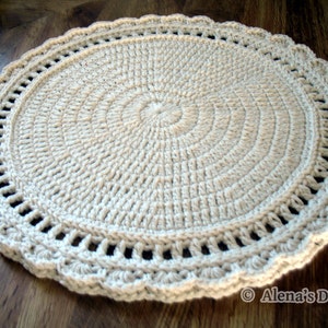 May include: A round, crocheted beige rug with a scalloped edge. The rug is made with a simple stitch pattern and has a delicate, lacy look.