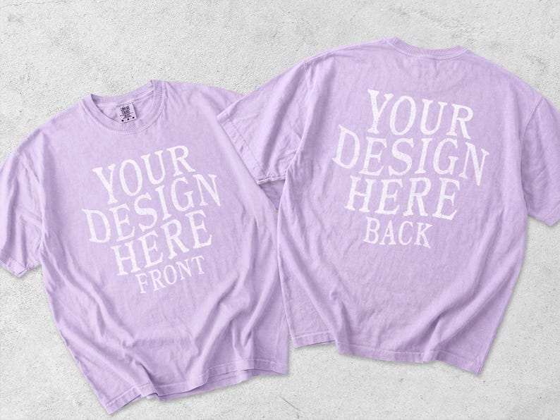 May include: Two light purple short-sleeve t-shirts displayed together. The left shirt features white text reading YOUR DESIGN HERE FRONT. The right shirt features white text reading YOUR DESIGN HERE BACK. Both shirts have a crew neckline.