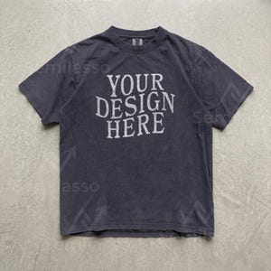 May include: A dark charcoal gray short-sleeve t-shirt with a crew neckline. The center of the chest features the white text "YOUR DESIGN HERE" in a distressed, serif font. The fabric has a slightly faded, washed-out appearance throughout.