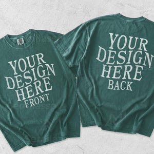 May include: Two dark teal short-sleeve t-shirts displayed together. The left shirt features the white text YOUR DESIGN HERE FRONT. The right shirt displays the white text YOUR DESIGN HERE BACK. Both garments have a crew neckline and a relaxed fit.