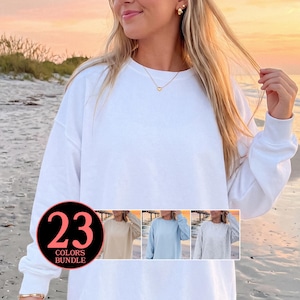 May include: A white crew neck sweatshirt with long sleeves. The image includes a colour bundle graphic with the text "23 COLORS BUNDLE". The background shows a beach scene with a sunset.
