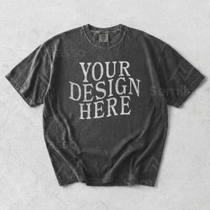 Puede incluir: Camiseta gris oscuro con el texto blanco "YOUR DESIGN HERE" en letras desgastadas. La camiseta tiene un aspecto vintage y lavado, con cuello redondo. Esta camiseta de manga corta es de estilo unisex.