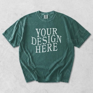 May include: A teal-colored t-shirt with the text "YOUR DESIGN HERE" in white, centered on the front. The shirt has a crew neck and short sleeves. The fabric appears to be slightly faded.