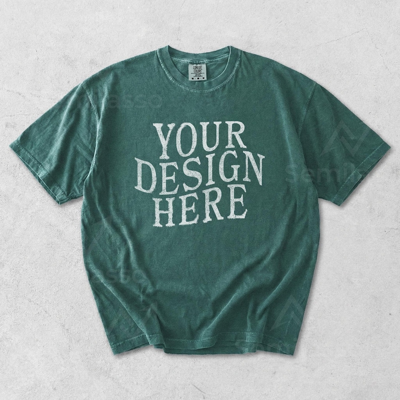 May include: A teal-colored t-shirt with the text "YOUR DESIGN HERE" in white, centered on the front. The shirt has a crew neck and short sleeves. The fabric appears to be slightly faded.