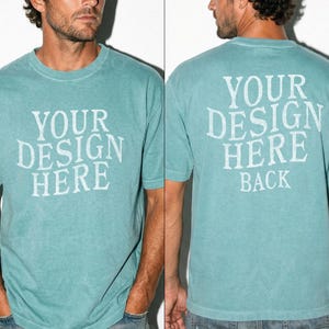May include: A teal-colored t-shirt with the text "YOUR DESIGN HERE" printed on the front and "YOUR DESIGN HERE BACK" on the back. The shirt has short sleeves and a crew neck. The fabric appears to be slightly faded.