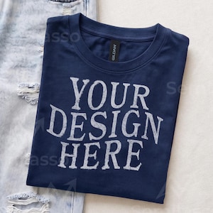 May include: A navy blue crew neck t-shirt featuring the white distressed text "YOUR DESIGN HERE" printed on the front. The shirt has a Gildan brand label at the inner neckline and is positioned next to a pair of light blue distressed denim jeans.