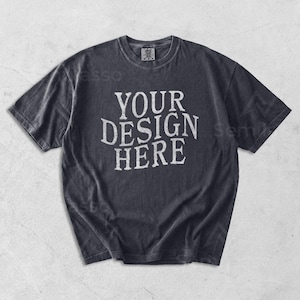 May include: A dark gray t-shirt with the text "YOUR DESIGN HERE" in a distressed white font. The shirt has a crew neck and short sleeves. The fabric appears to be pre-washed for a vintage look.