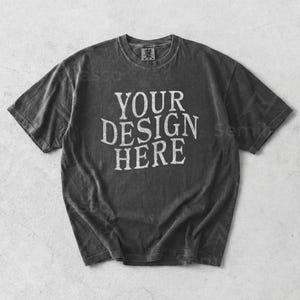 May include: A charcoal gray t-shirt with the text "YOUR DESIGN HERE" in white, distressed lettering. The shirt has a crew neck and short sleeves. The fabric appears to be pre-shrunk and slightly faded.