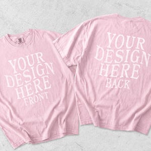 May include: Two light pink short-sleeve t-shirts displayed together. The left shirt features white text reading YOUR DESIGN HERE FRONT. The right shirt features white text reading YOUR DESIGN HERE BACK. Both shirts have a crew neckline.