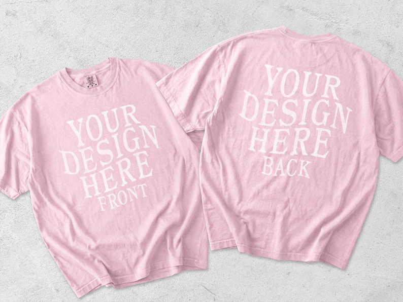 May include: Two light pink short-sleeve t-shirts displayed together. The left shirt features white text reading YOUR DESIGN HERE FRONT. The right shirt features white text reading YOUR DESIGN HERE BACK. Both shirts have a crew neckline.