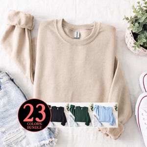 May include: A solid beige crewneck sweatshirt with long sleeves and a ribbed collar. A circular graphic overlay displays the text 23 COLORS BUNDLE and shows three additional sweatshirt variations in black, dark green, and light blue colours.