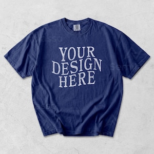 May include: A navy blue t-shirt with the text "YOUR DESIGN HERE" in a distressed white font. The short-sleeved shirt is made of a soft material and has a crew neck. The shirt is a blank canvas for custom designs.