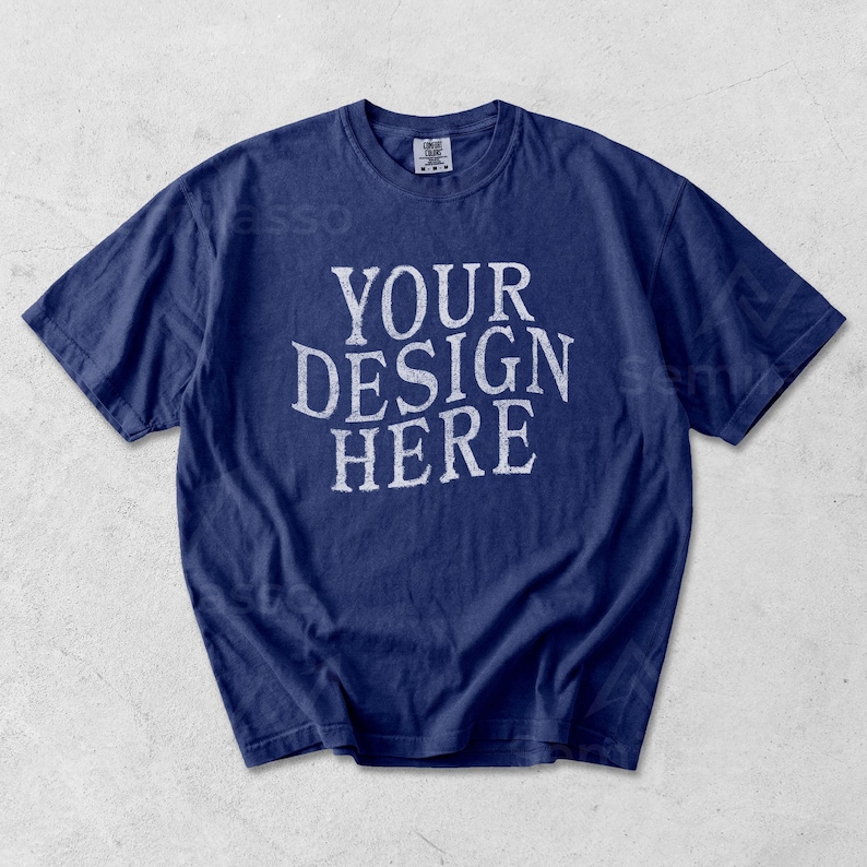 May include: A navy blue t-shirt with the text "YOUR DESIGN HERE" in a distressed white font. The short-sleeved shirt is made of a soft material and has a crew neck. The shirt is a blank canvas for custom designs.
