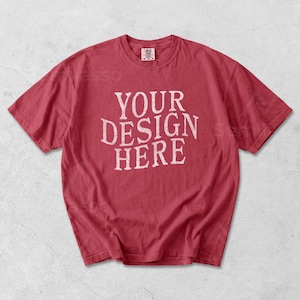 May include: Red t-shirt with the text "YOUR DESIGN HERE" in a distressed white font. The shirt has a crew neck and short sleeves. The fabric appears soft and slightly faded, suggesting a vintage or worn look.