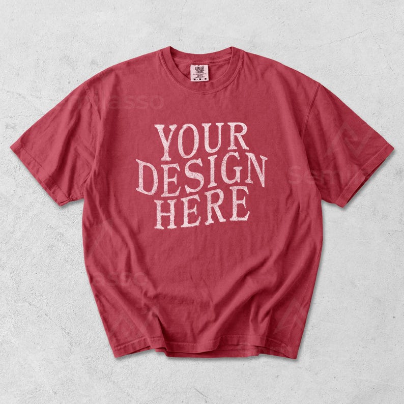 May include: Red t-shirt with the text "YOUR DESIGN HERE" in a distressed white font. The shirt has a crew neck and short sleeves. The fabric appears soft and slightly faded, suggesting a vintage or worn look.