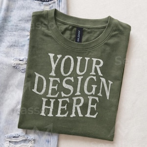 May include: An olive green crew neck t-shirt with the white text YOUR DESIGN HERE printed on the front. The shirt features a Gildan brand label at the inner neckline and is positioned next to a pair of light blue distressed denim jeans.