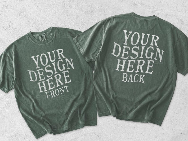May include: Two sage green short-sleeve t-shirts displayed flat. The left shirt features the white text YOUR DESIGN HERE FRONT. The right shirt displays the white text YOUR DESIGN HERE BACK. Both garments have a crew neckline and a vintage wash.