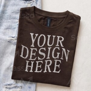 May include: A dark brown short-sleeved t-shirt with a crew neckline and the white text "YOUR DESIGN HERE" printed in a distressed font on the front. The shirt features a black Gildan brand label inside the collar and is folded neatly.