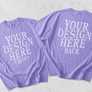 May include: Two light purple short-sleeve t-shirts displayed together. The left shirt features the white text YOUR DESIGN HERE FRONT. The right shirt shows the back side with the white text YOUR DESIGN HERE BACK. Both shirts have a crew neckline.