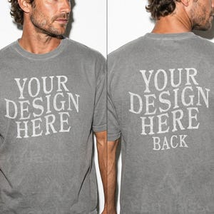 May include: A gray t-shirt with the text "YOUR DESIGN HERE" printed on the front and back in a distressed white font. The shirt has a crew neck and short sleeves. The fabric appears to be pre-washed.