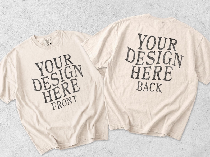 May include: Two off-white short-sleeve t-shirts displayed together. The left shirt features dark gray text reading YOUR DESIGN HERE FRONT. The right shirt features dark gray text reading YOUR DESIGN HERE BACK. Both shirts have a crew neckline.