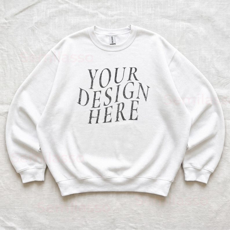 Puede incluir: Una sudadera blanca de cuello redondo con el texto negro "YOUR DESIGN HERE" impreso en una fuente serif desgastada en el centro del pecho. La prenda tiene mangas largas con pu&ntilde;os y dobladillo acanalados, presentando un estilo cl&aacute;sico.