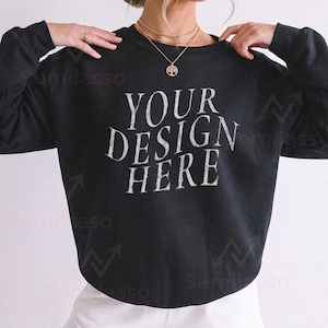 May include: A black long-sleeve crewneck sweatshirt featuring the white text "YOUR DESIGN HERE" printed in a distressed, serif font across the chest. The garment has a standard fit with ribbed cuffs and a ribbed neckline, worn with white shorts.