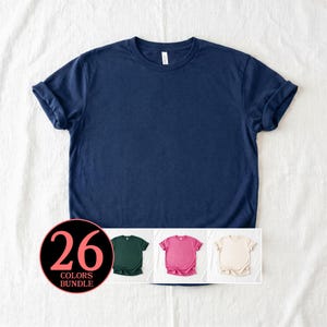 Può includere: Una t-shirt blu navy a maniche corte con scollo rotondo e maniche arrotolate. Un grafico circolare nell'angolo mostra il testo 26 COLORS BUNDLE, con piccole immagini di una t-shirt verde scuro, una rosa e una color crema sottostanti.
