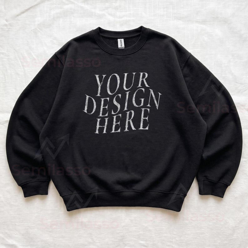 Puede incluir: Una sudadera negra de manga larga con cuello redondo que presenta el texto blanco de estilo desgastado "YOUR DESIGN HERE" impreso en el centro del pecho. La prenda tiene cuello, pu&ntilde;os y dobladillo acanalados, corte est&aacute;ndar y etiqueta Gildan.