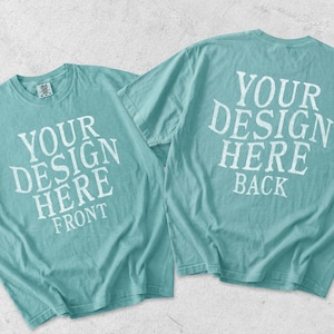 May include: Two teal short-sleeve t-shirts displayed together. The left shirt features white text reading YOUR DESIGN HERE FRONT. The right shirt displays white text reading YOUR DESIGN HERE BACK. Both shirts have a crew neckline and a relaxed fit.