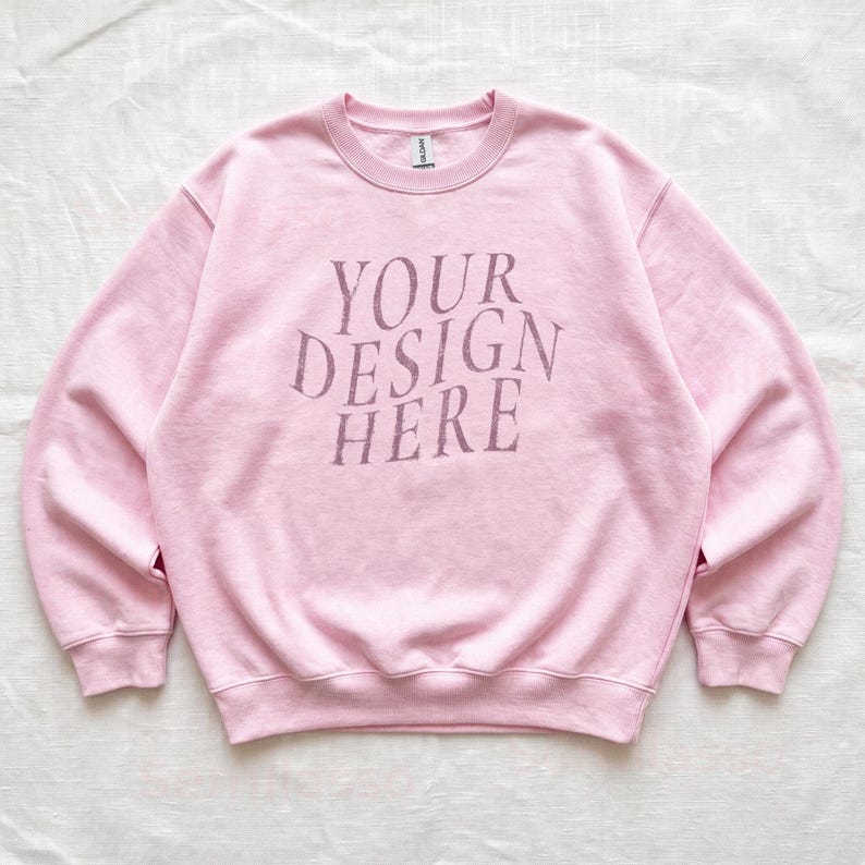 Puede incluir: Una sudadera de cuello redondo en color rosa claro con mangas largas y bordes acanalados en el cuello, pu&ntilde;os y dobladillo. En el centro del pecho aparece el texto "YOUR DESIGN HERE" en una tipograf&iacute;a serif de color rosa oscuro desgastada.