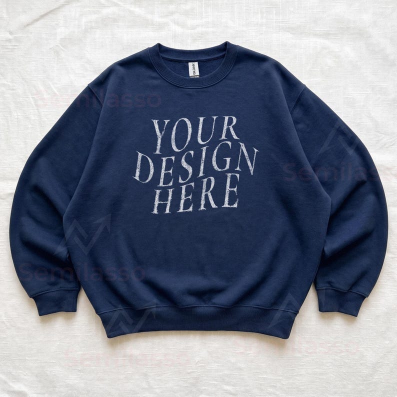 Puede incluir: Una sudadera azul marino de cuello redondo con el texto blanco "YOUR DESIGN HERE" impreso en una fuente serif desgastada en el pecho. La prenda tiene mangas largas, cuello y pu&ntilde;os acanalados, con una etiqueta de la marca Gildan en el cuello.