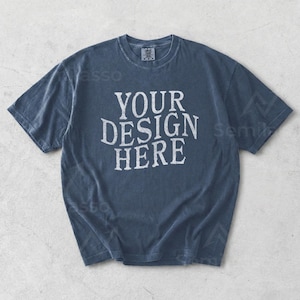 May include: A faded blue t-shirt with the text "YOUR DESIGN HERE" in a distressed white font. The short-sleeved shirt has a crew neck and a relaxed fit, suitable for casual wear. The shirt is made of a soft, comfortable material.