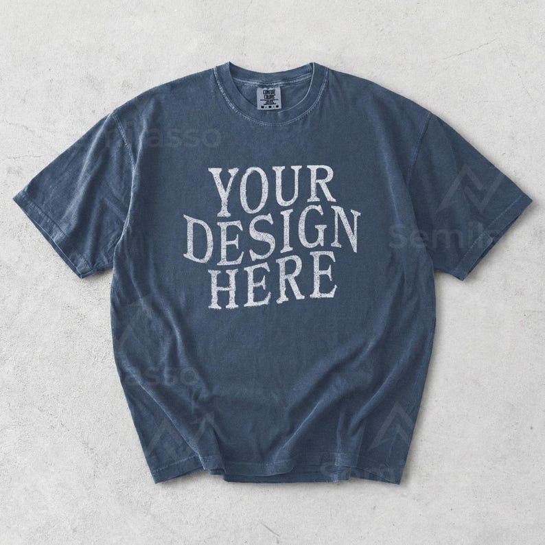 May include: A faded blue t-shirt with the text "YOUR DESIGN HERE" in a distressed white font. The short-sleeved shirt has a crew neck and a relaxed fit, suitable for casual wear. The shirt is made of a soft, comfortable material.