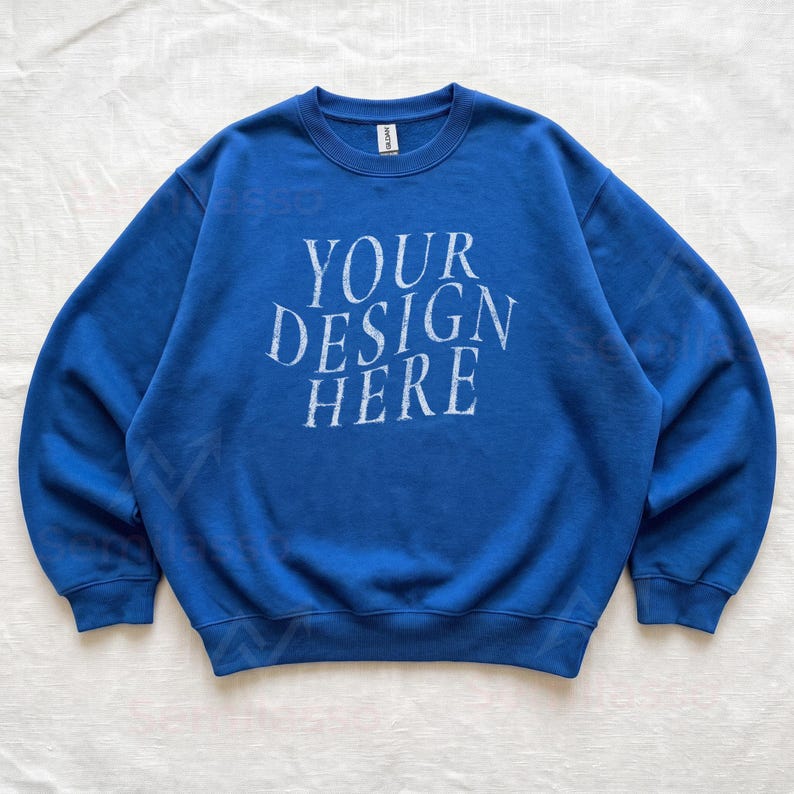 Puede incluir: Una sudadera azul real de cuello redondo con el texto blanco desgastado "YOUR DESIGN HERE" impreso en el centro del pecho. La prenda tiene mangas largas con pu&ntilde;os acanalados, un dobladillo acanalado y un cuello acanalado con etiqueta.