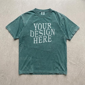 May include: A short-sleeve crew neck t-shirt in a muted teal green color with a vintage-style wash. The center of the chest features the white text "YOUR DESIGN HERE" in a bold, serif font. The garment has a standard fit and a ribbed collar.