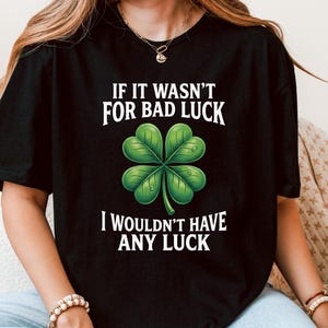 Könnte beinhalten: Schwarzes T-Shirt mit dem weißen Text "IF IT WASN'T FOR BAD LUCK I WOULDN'T HAVE ANY LUCK". Eine grüne vierblättrige Kleeblatt-Grafik ist mittig auf dem Shirt. Das Shirt besteht aus einem weichen Material.