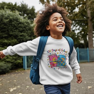 May include: A white sweatshirt featuring a colorful graphic that reads "100 Days of School." The graphic includes two smiling books tied with a bow, stars, and other decorative elements. The sweatshirt is worn by a child with a blue backpack.
